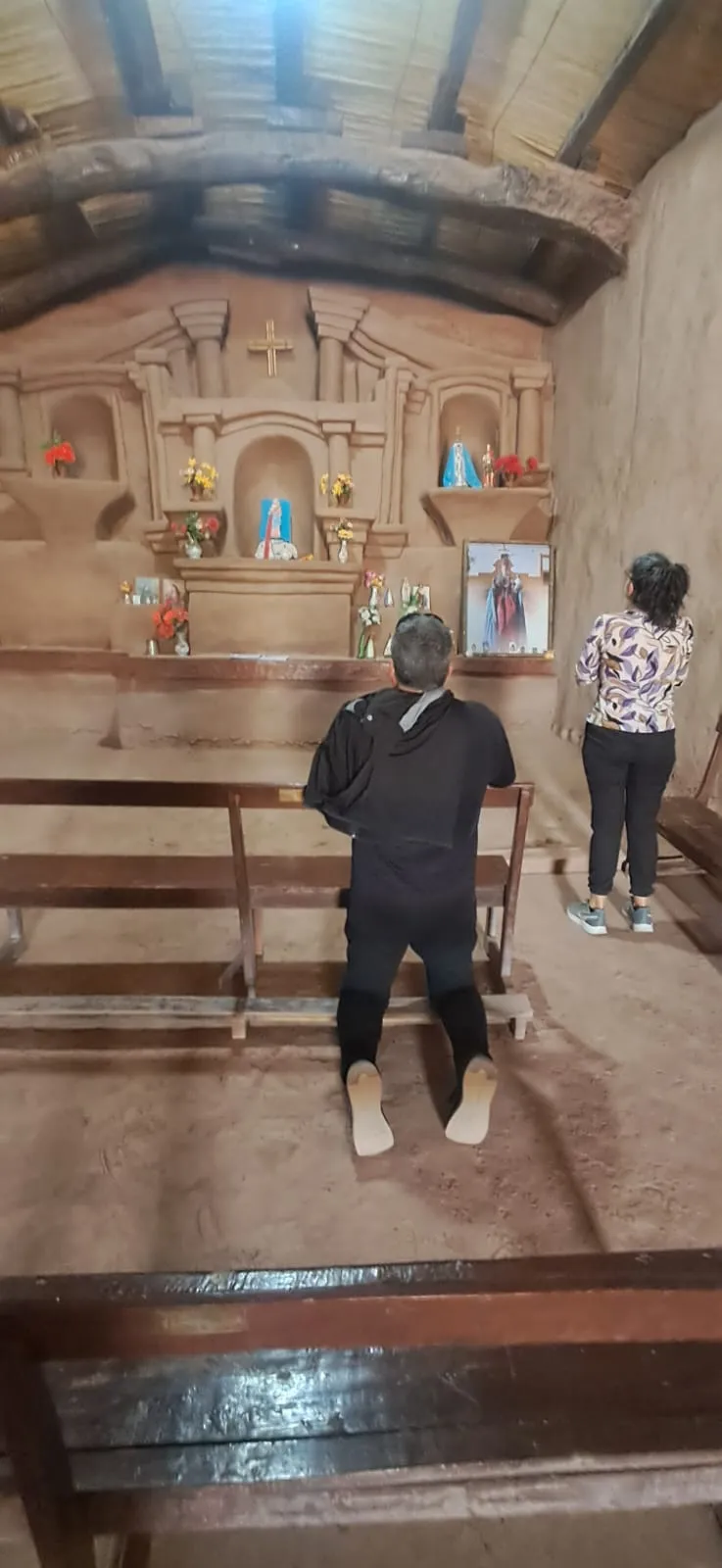 Interior de la capilla de Nuestra Señora del Rosario, con su altar de barro y dos visitantes de espaldas