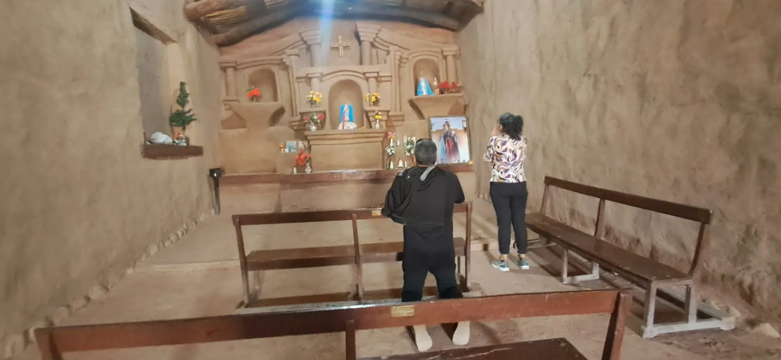 Interior de la capilla de Nuestra Señora del Rosario, con bancos de madera, el altar al fondo y dos visitantes