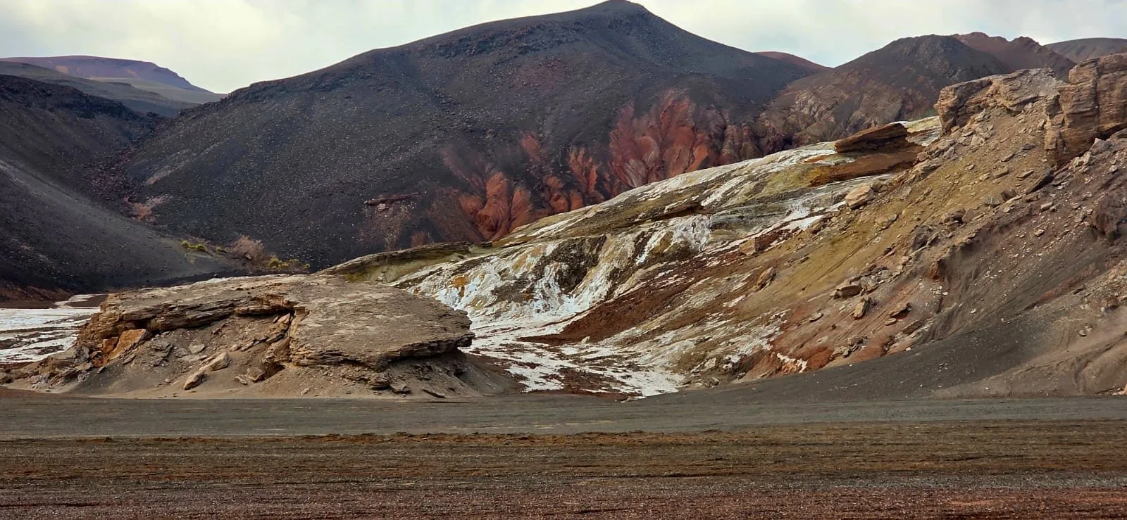Cerros oscuros y rojizos con vetas blancas de sal sobre una llanura de la puna