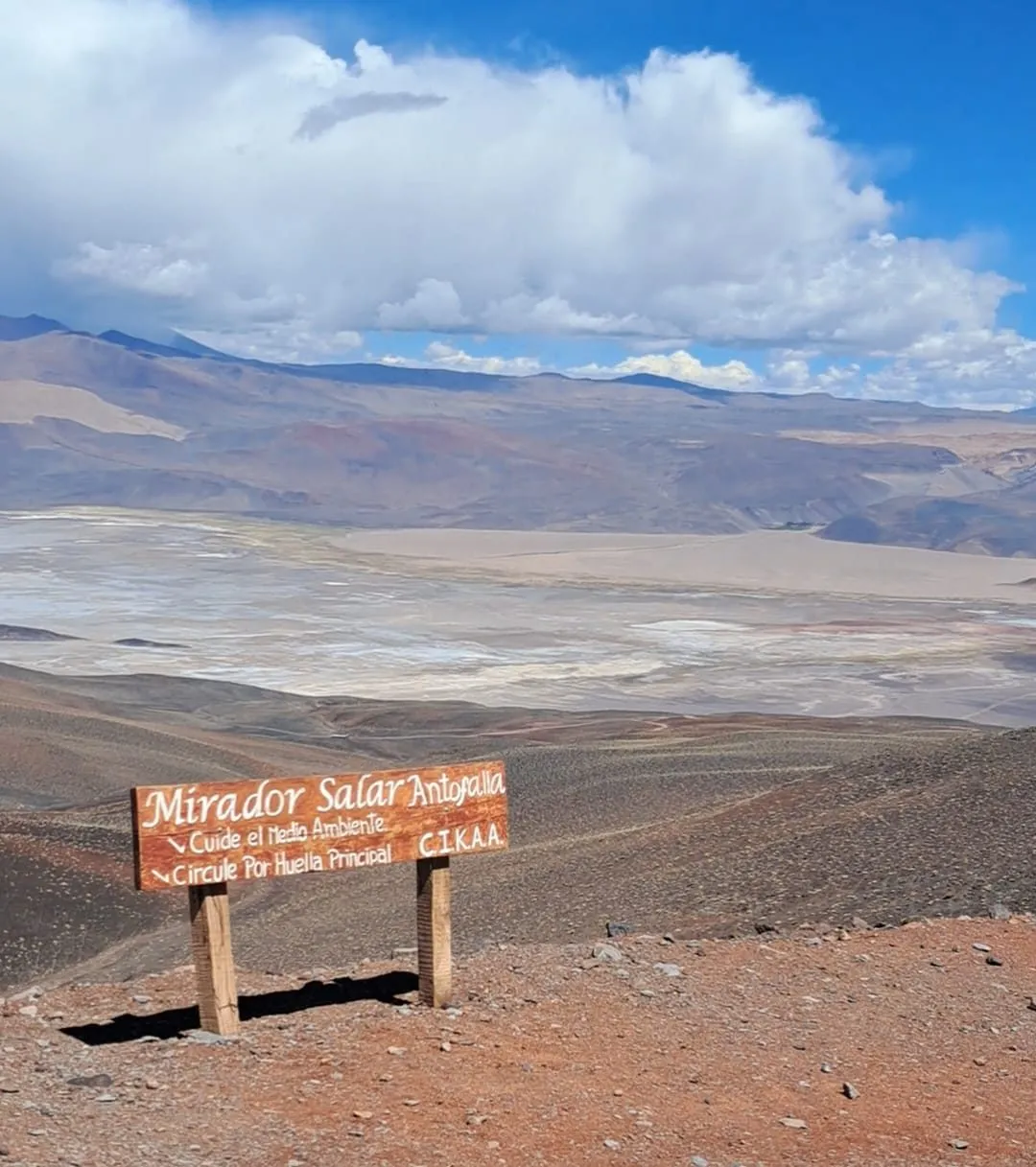 Cartel del Mirador del Salar de Antofalla sobre una loma rojiza, con el salar blanco abajo