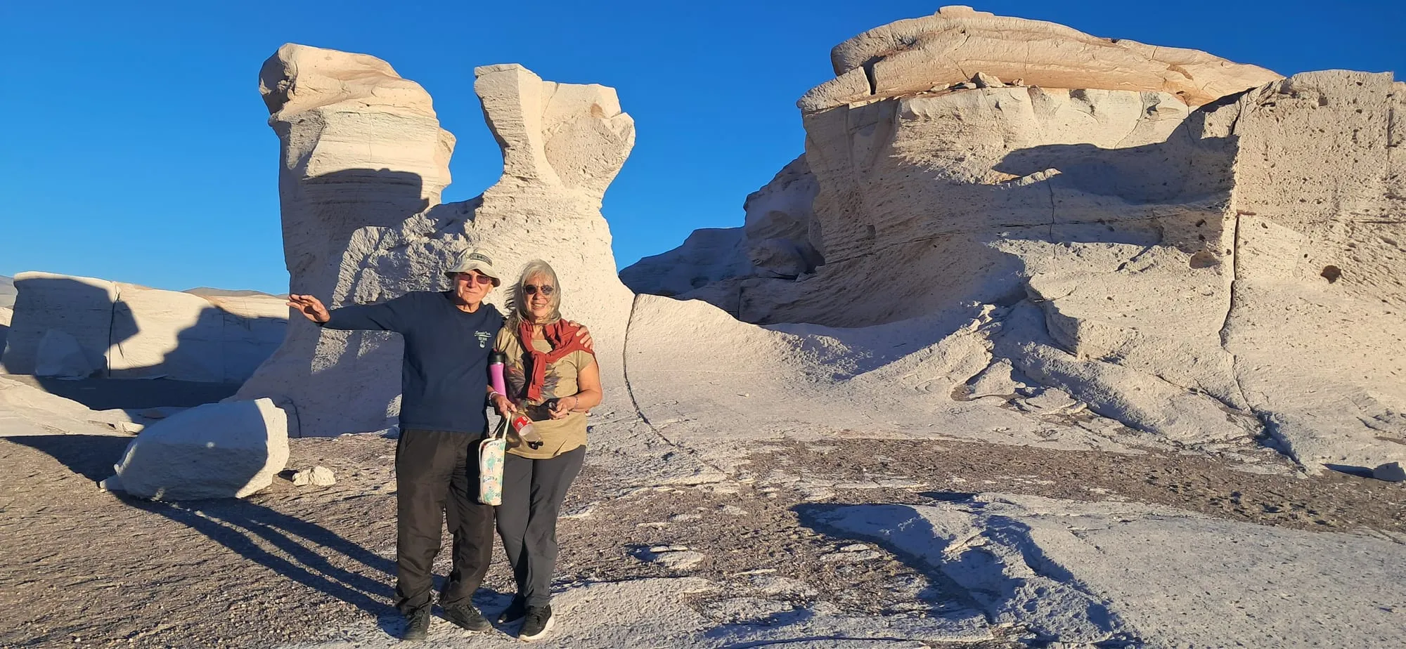 Una pareja entre grandes formaciones blancas de piedra pómez, bajo un cielo azul