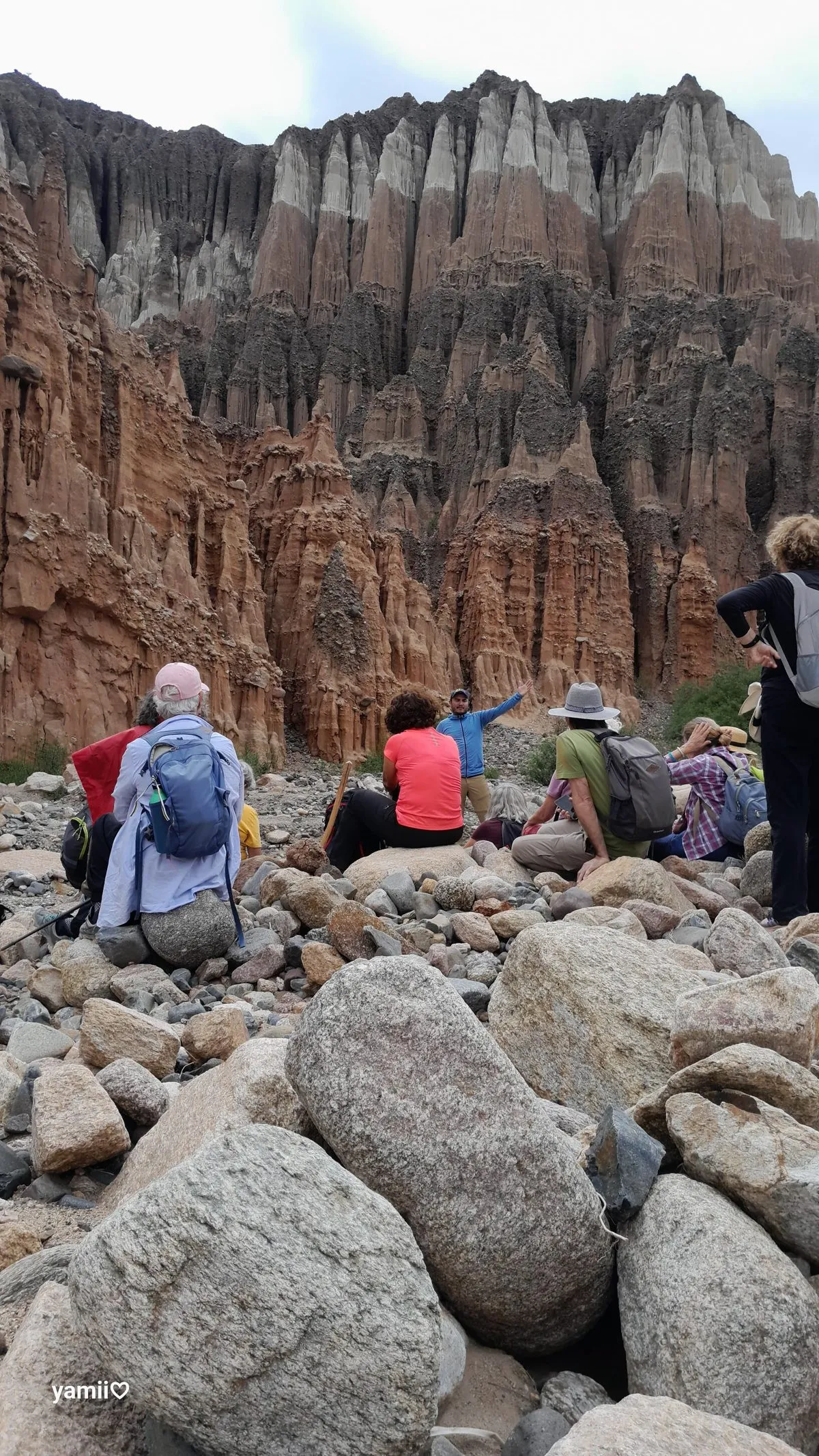 Viajeros descansando sobre grandes piedras frente a una muralla de roca con torres