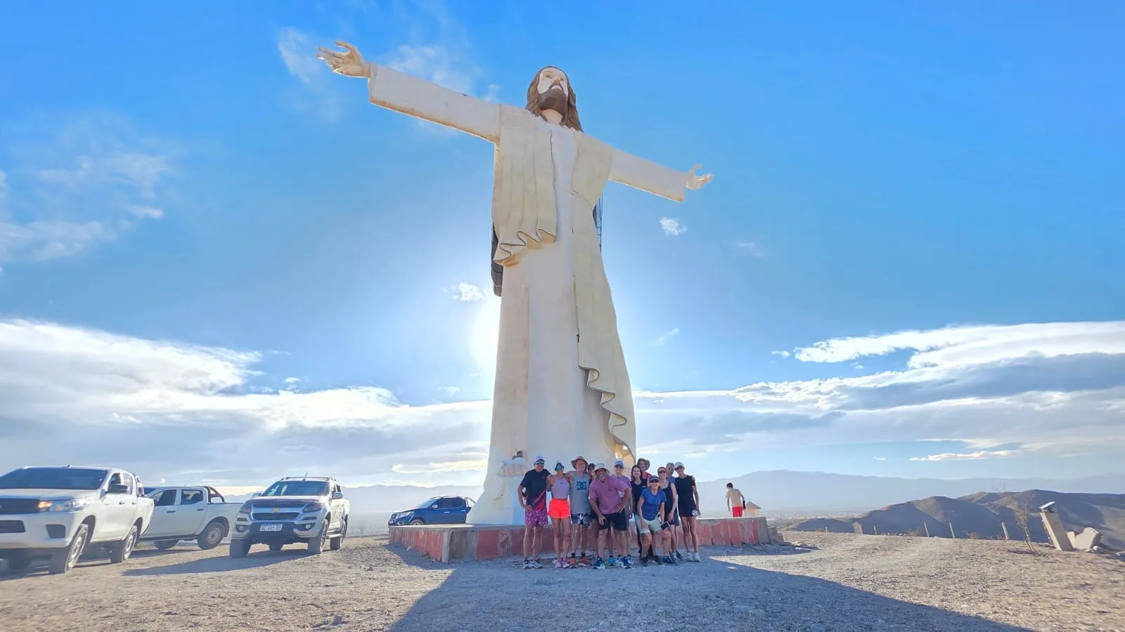 Gran estatua de Cristo con los brazos abiertos y varias camionetas 4x4 estacionadas al pie
