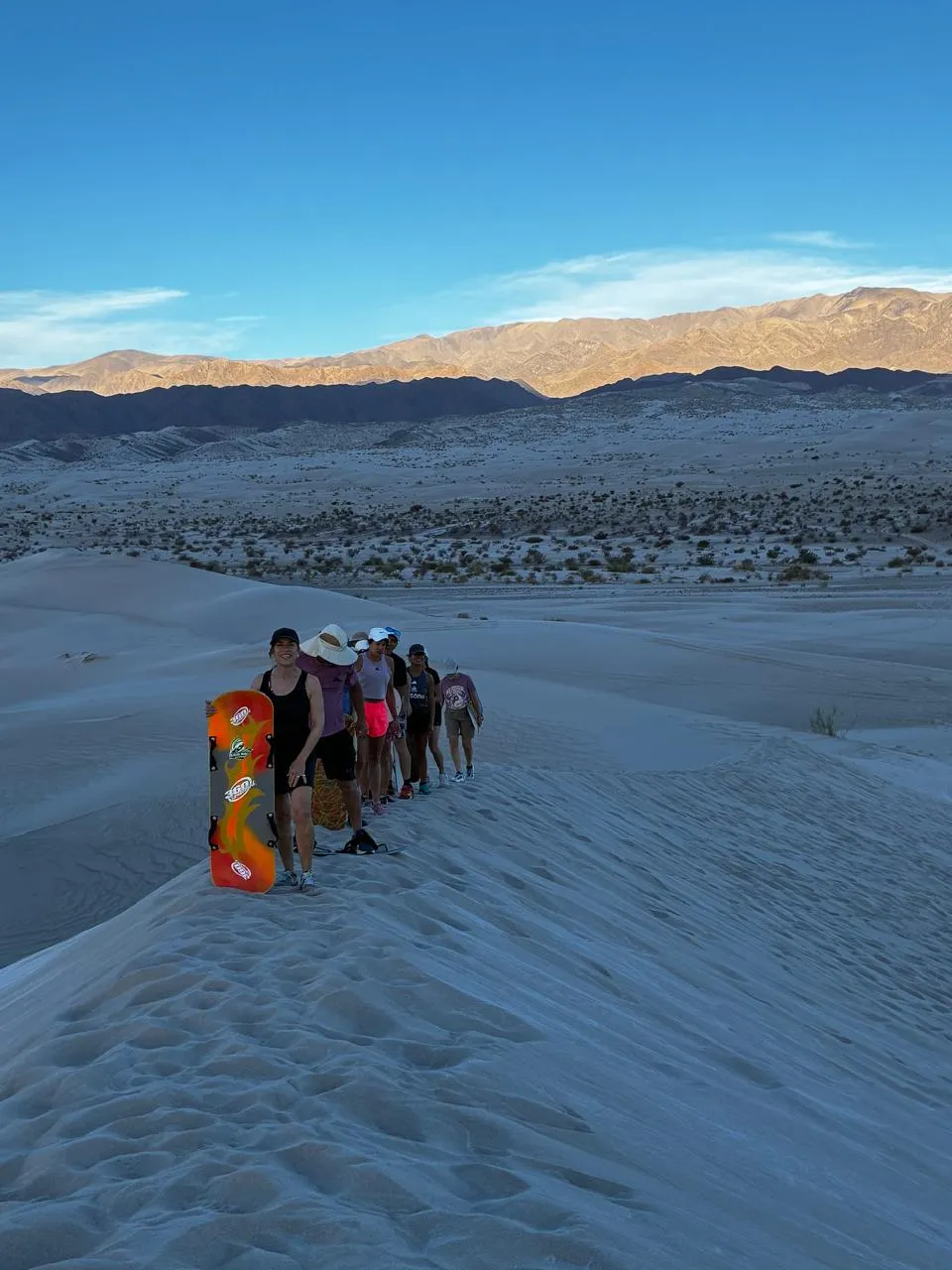 Una fila de personas con tablas de sandboard sobre la cresta de una duna