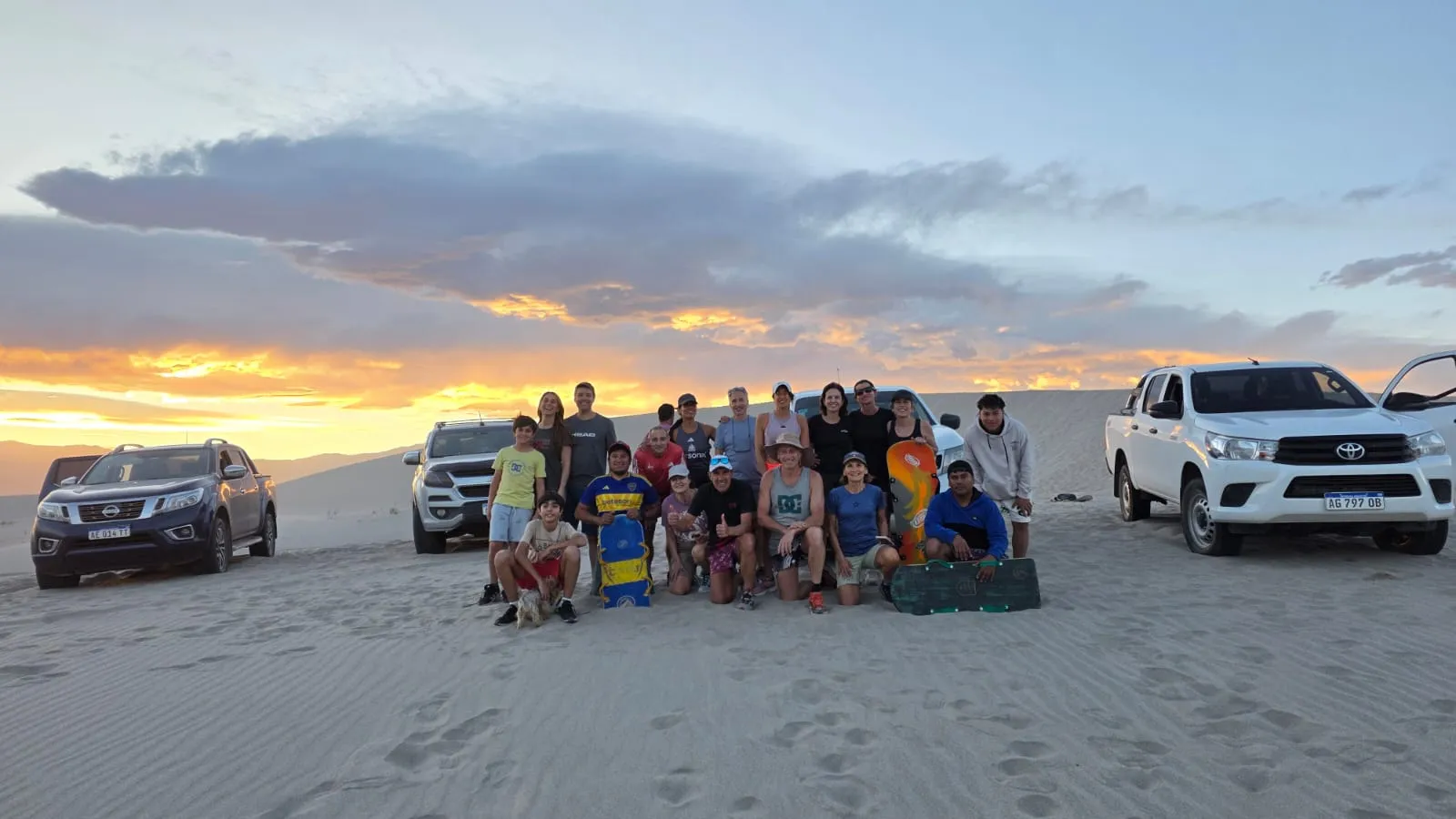 Un grupo de viajeros sentado entre camionetas 4x4 sobre la arena al atardecer