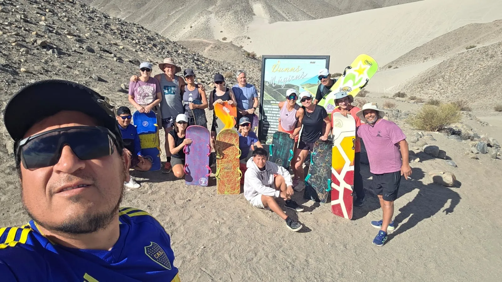 Un grupo numeroso de viajeros con tablas de sandboard posando entre dunas