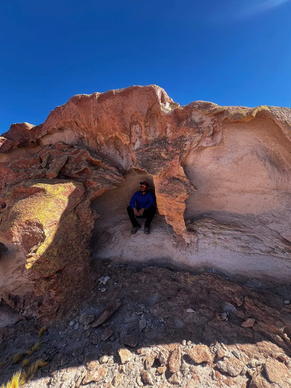 Una formación de roca anaranjada con una cueva baja bajo un cielo azul