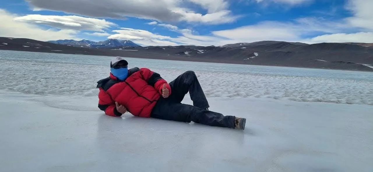 Una persona recostada sobre la superficie blanca de una laguna de altura, con cordillera al fondo