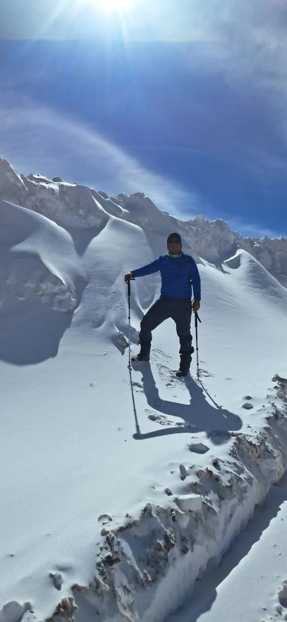 Un hombre con bastones de trekking parado sobre un manto de nieve bajo el sol