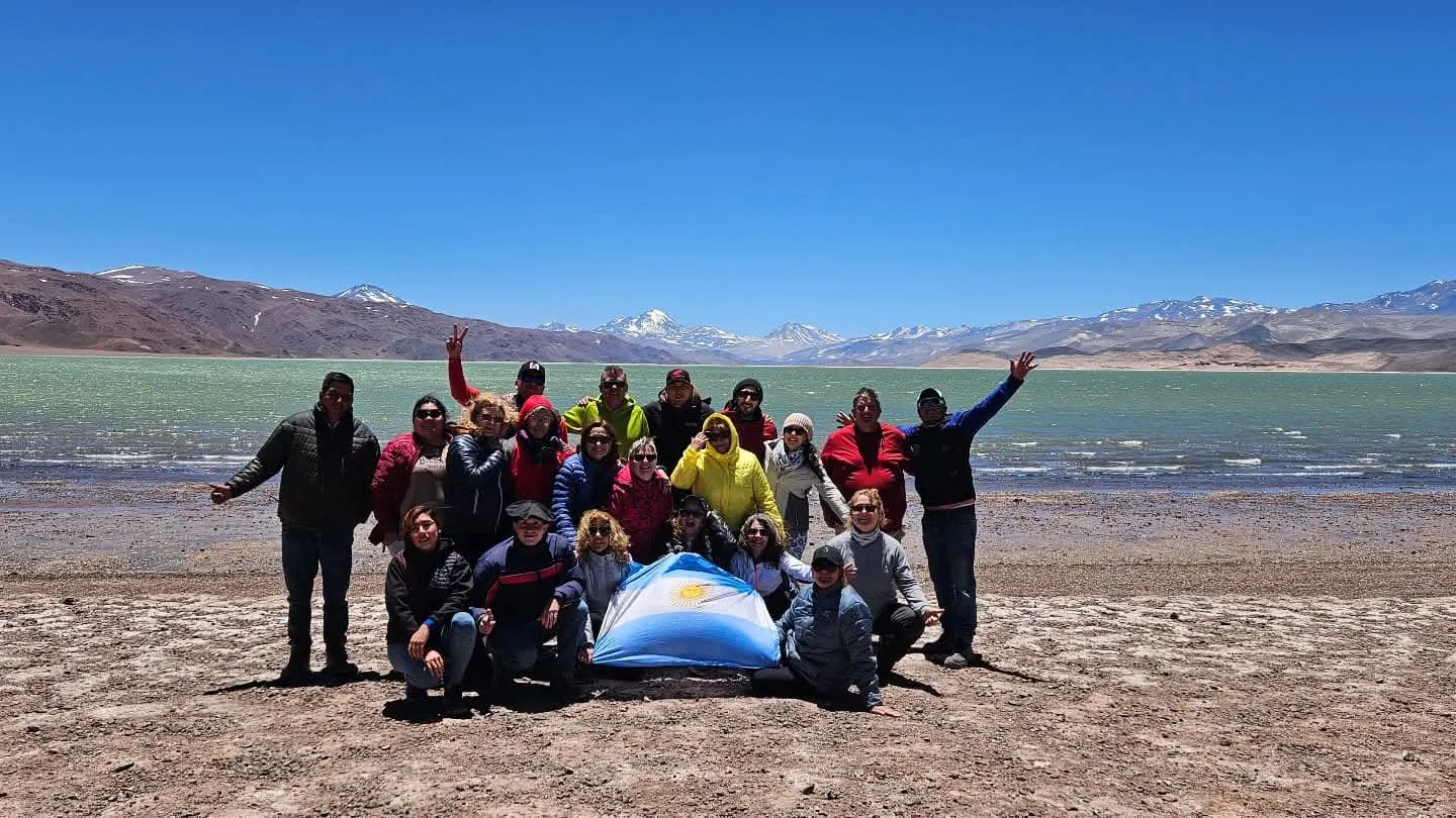 Un grupo de viajeros con una bandera argentina frente a una laguna de altura