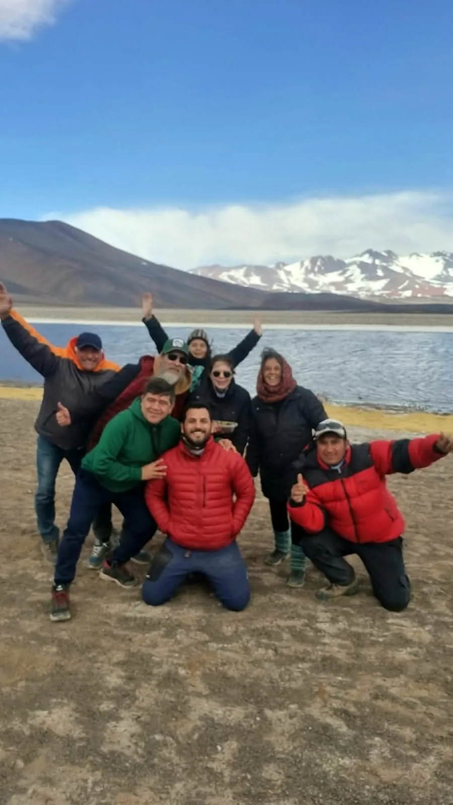 Un grupo de viajeros abrazados, con las manos en alto, a orillas de una laguna de altura