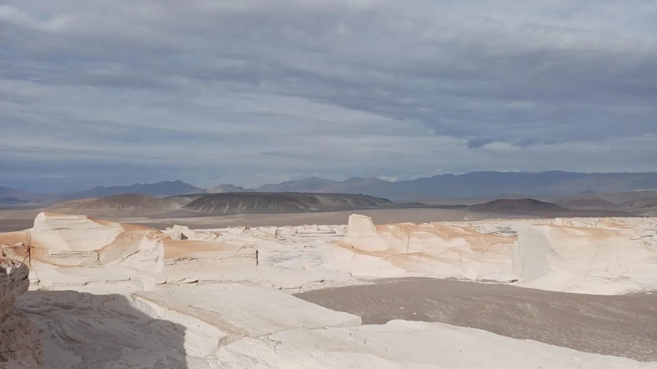 Cañón de piedra pómez blanca bajo un cielo nublado, con la cordillera al fondo