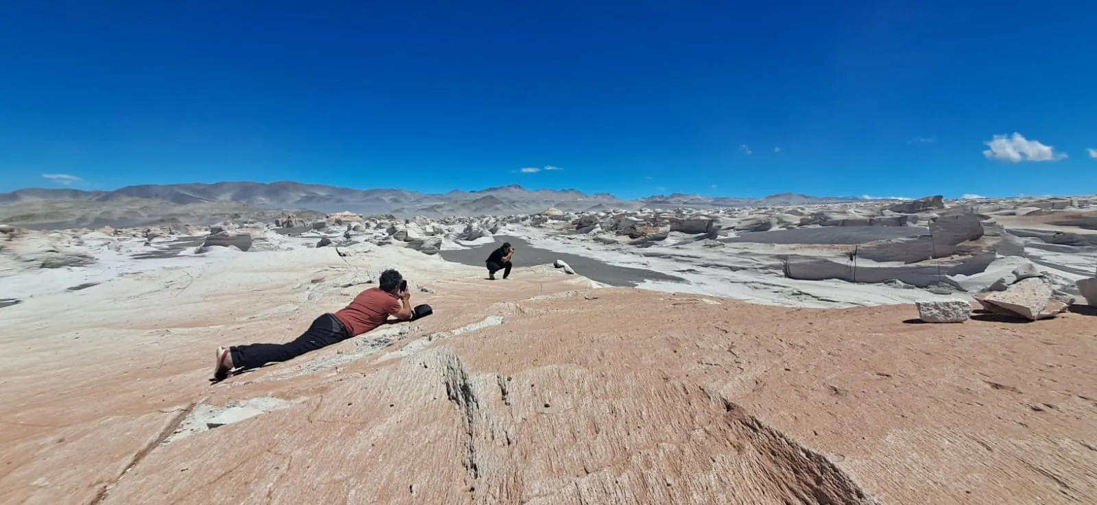 Una persona recostada sobre la roca rojiza, con el desierto blanco y la cordillera al fondo