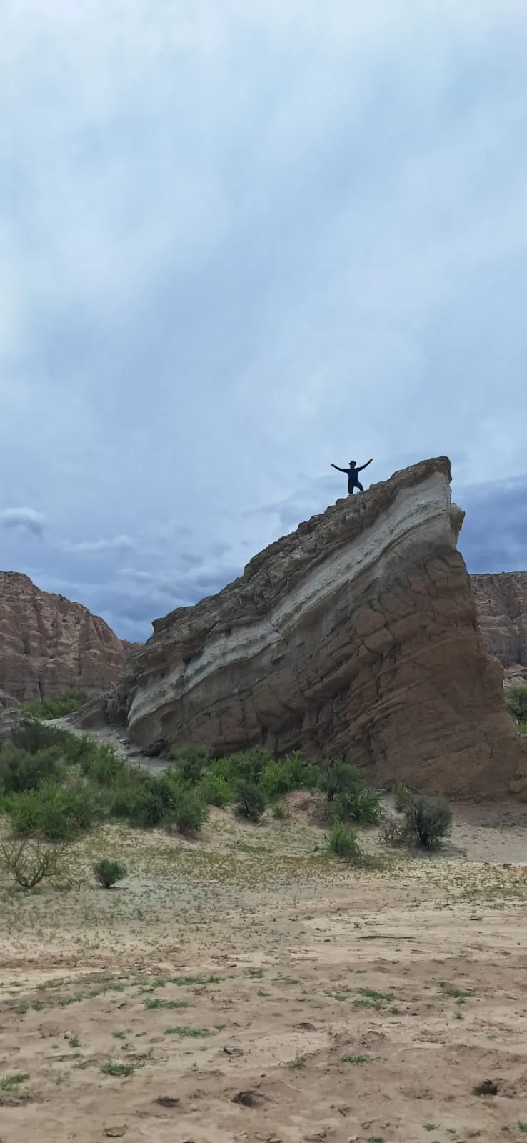 Una persona con los brazos en alto sobre la cima de una roca en capas, en la quebrada