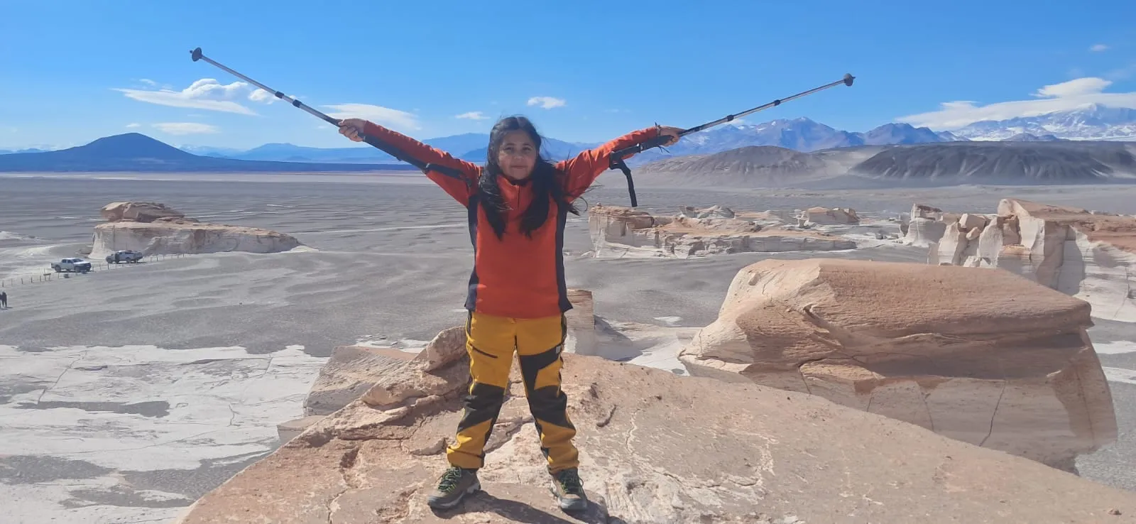 Una viajera con los brazos abiertos y bastones sobre una roca, frente al desierto blanco
