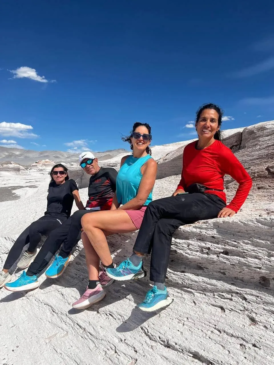 Cuatro viajeras sentadas sobre la roca blanca, con zapatillas turquesa y cielo azul