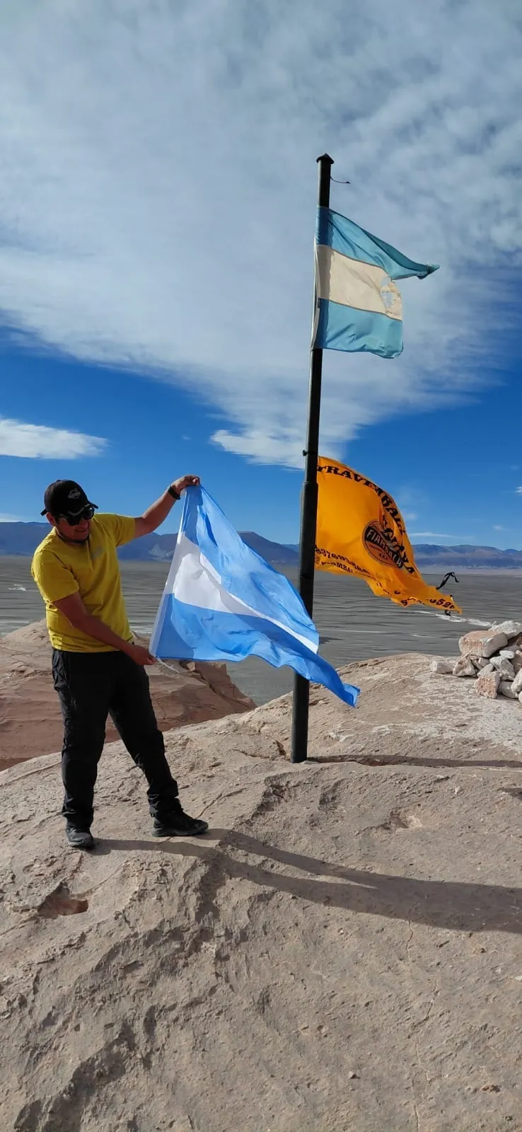 Un viajero sostiene la bandera argentina junto al mástil, en el Campo de Piedra Pómez