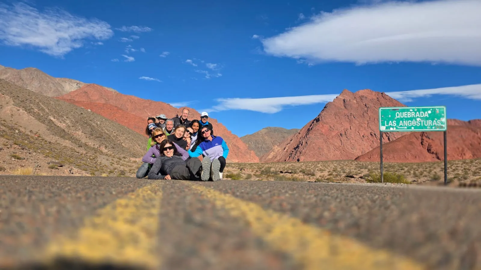 Cartel verde de la Quebrada Las Angosturas junto a la Ruta 60, con un cerro rojo detrás
