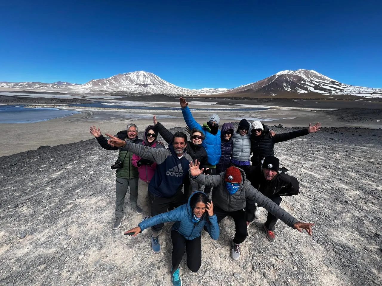 Un grupo de viajeros abrigados abrazados frente a la cordillera con nieve