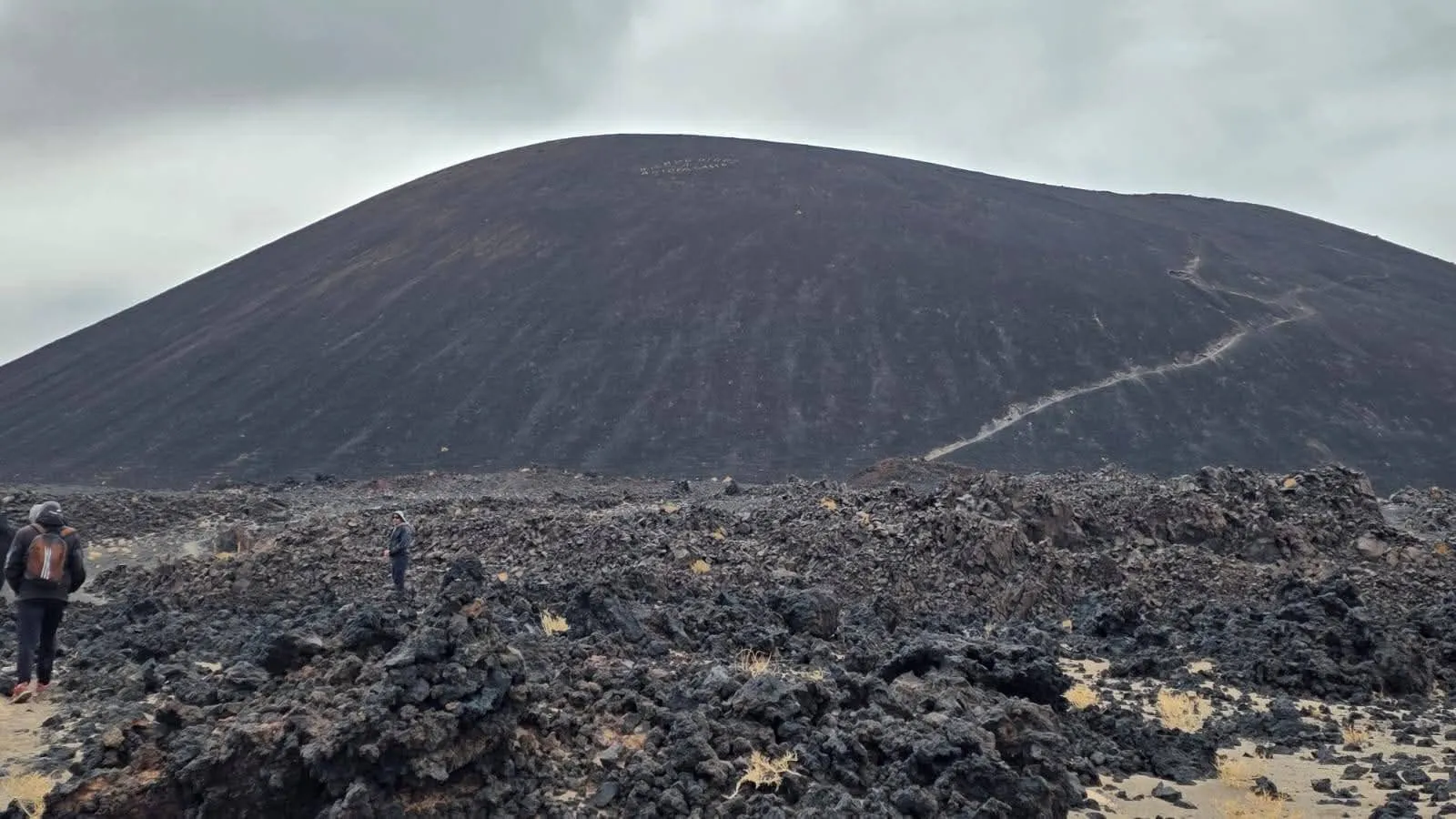 El cono oscuro del volcán Antofagasta con el sendero que sube hacia la cumbre, sobre un campo de lava