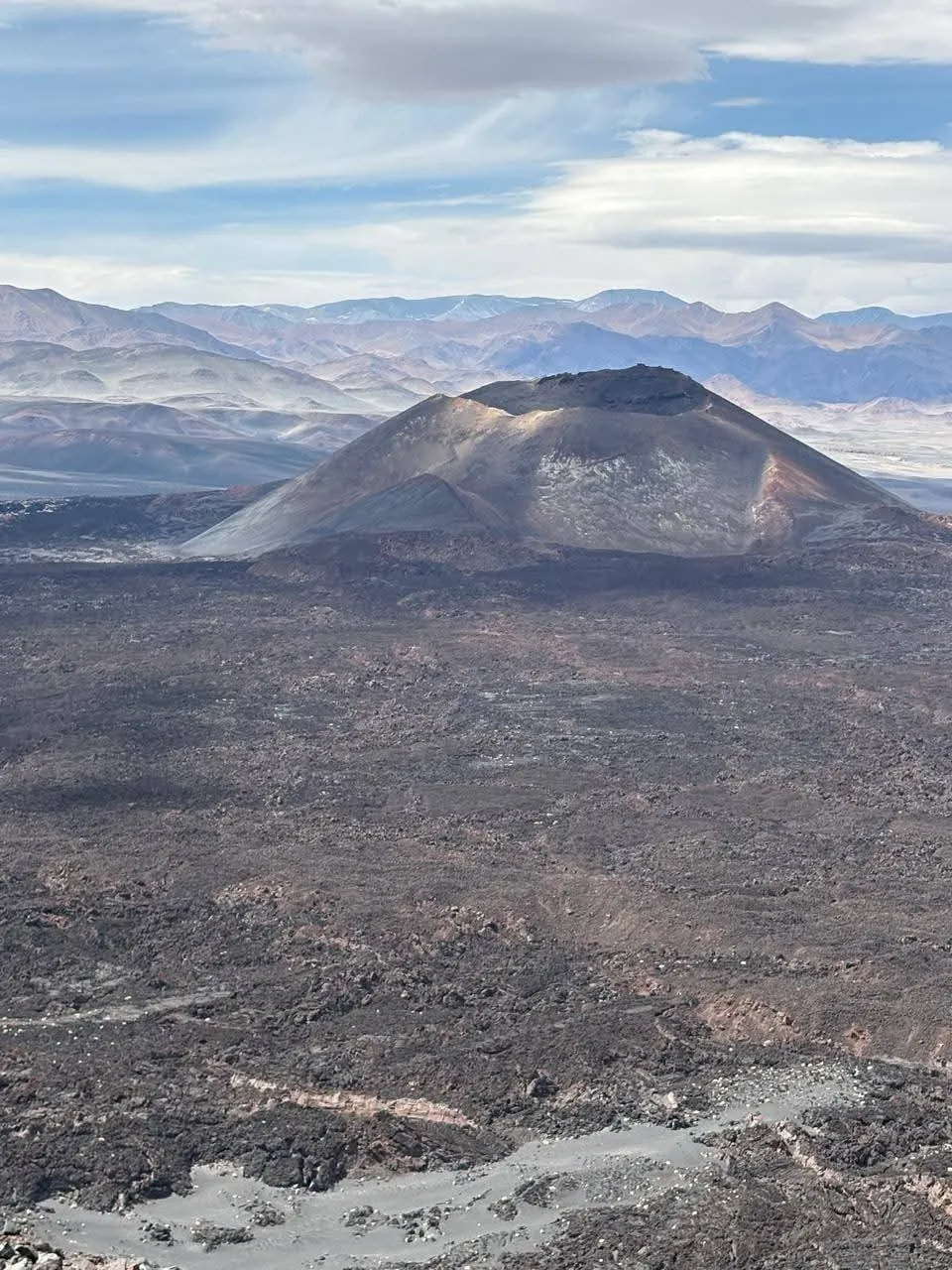 Cono volcánico rodeado de campo de lava negra y la cordillera al fondo