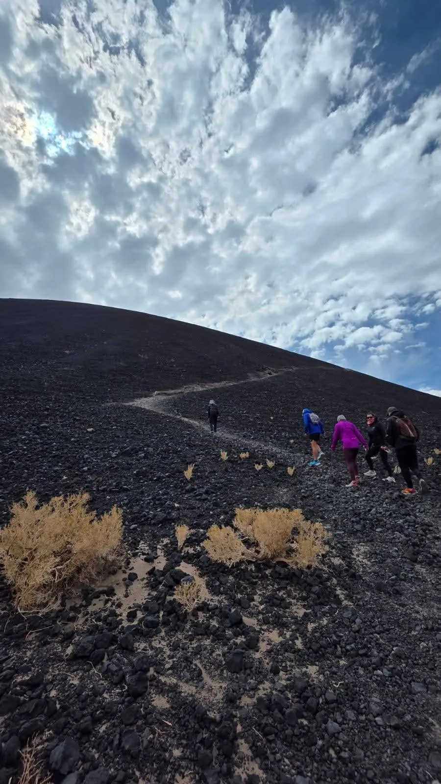Sendero que sube por la ladera de lava oscura, con un grupo de caminantes a lo lejos