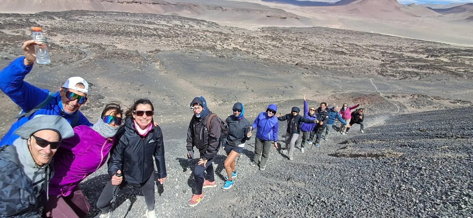 Una fila de caminantes con camperas de colores subiendo por la ladera del volcán