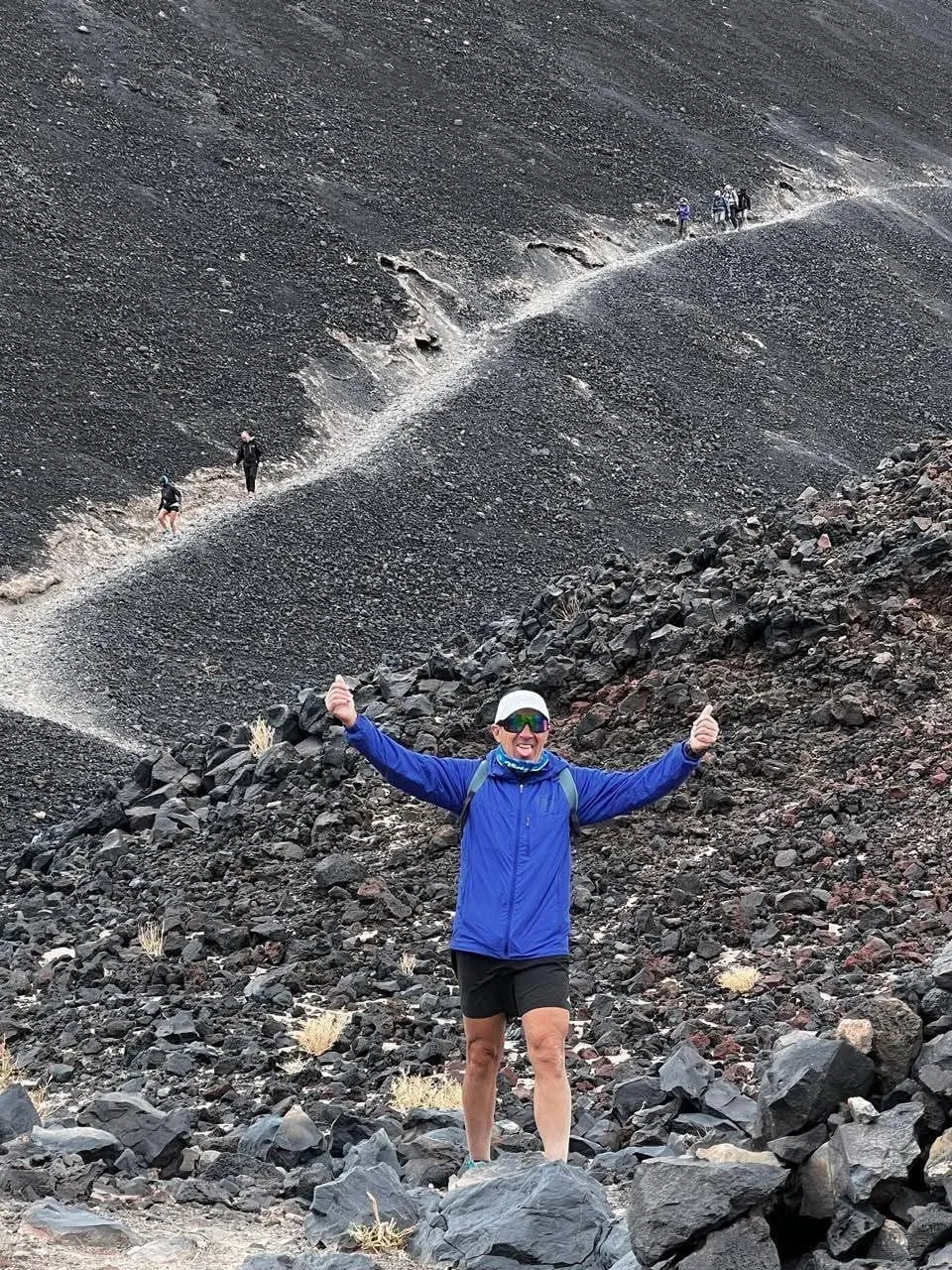 Un viajero con los brazos en alto sobre la ladera de piedra oscura del volcán
